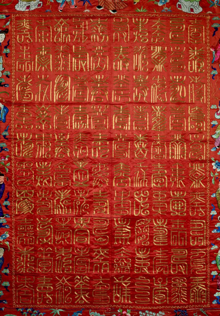 Chinese writing in gold thread forms a neat rectangle in the tapestry's center.