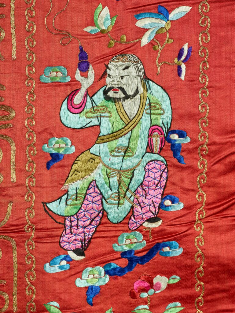 On the tapestry, a male with a short beard looks behind him while stepping forward with a purple bottle in his hand.
