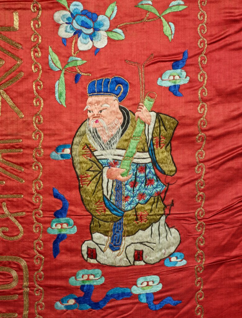 On the tapestry, an elderly man dressed in green, blue, and red carries a musical instrument.