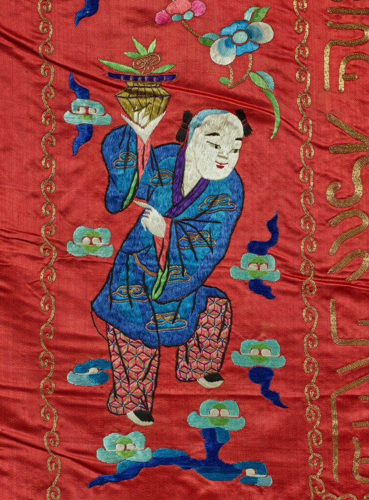 On the tapestry, a figure dressed in blue and red smiles while holding a flower basket with one leg raised.