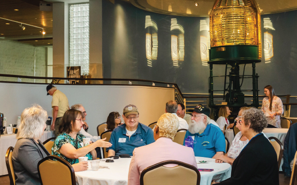 Mariners' staff and guests engaging in conversation around a round table in the Lower Lobby of the Museum.