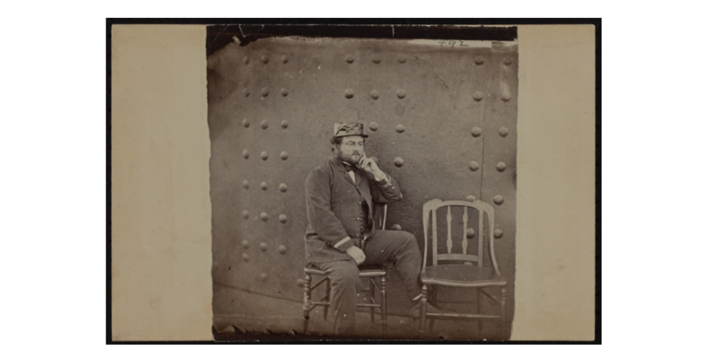 A picture of a uniformed man sitting in a chair, posing contemplatively