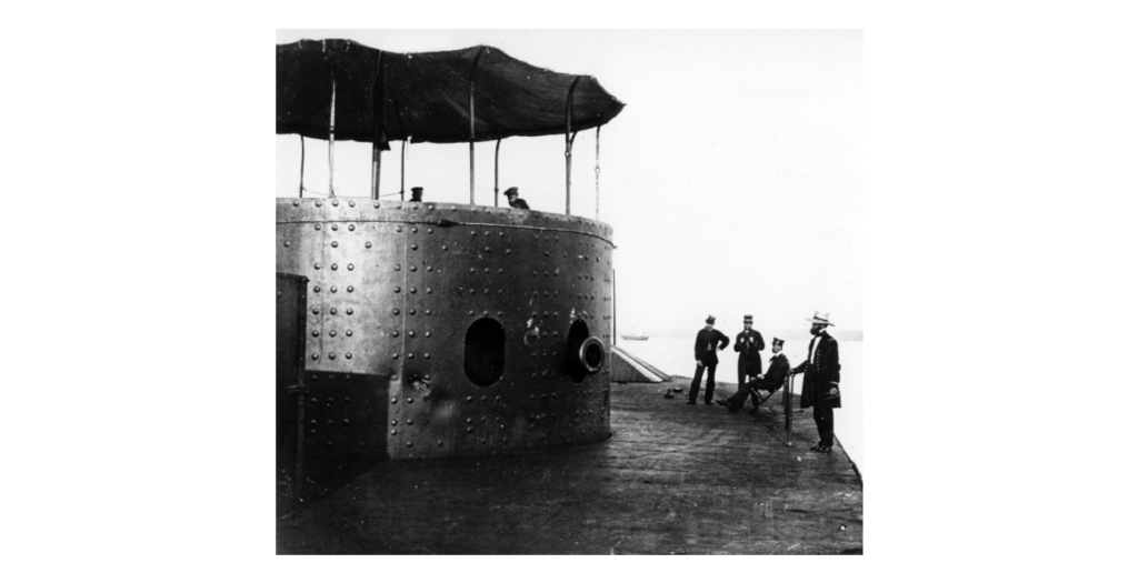 A picture of 4 men on deck outside of a turret looking into the turret at 2 men.