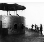 A picture of 4 men on deck outside of a turret looking into the turret at 2 men.