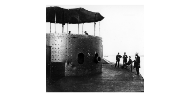 A picture of 4 men on deck outside of a turret looking into the turret at 2 men.