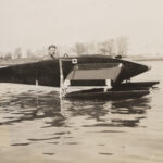 A man looks out from the cockpit of a boat on the water.