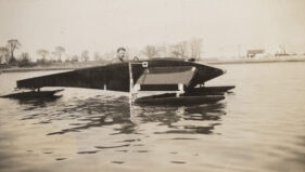 A man looks out from the cockpit of a boat on the water.