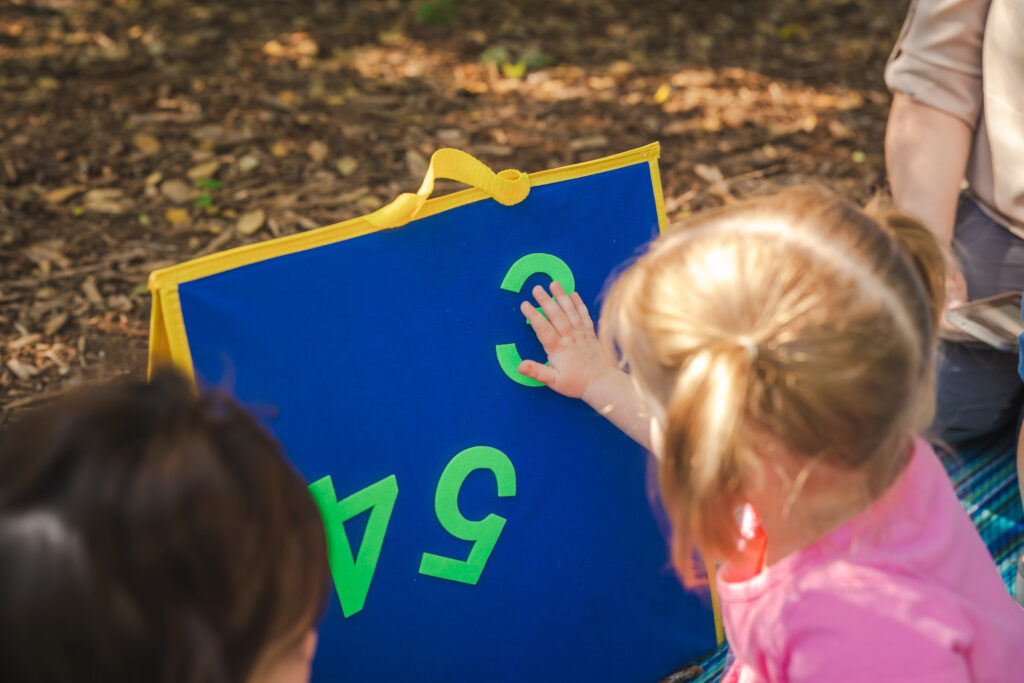 A small child touches the letter 3 on a blue and yellow board that also has the numbers 5 and 4