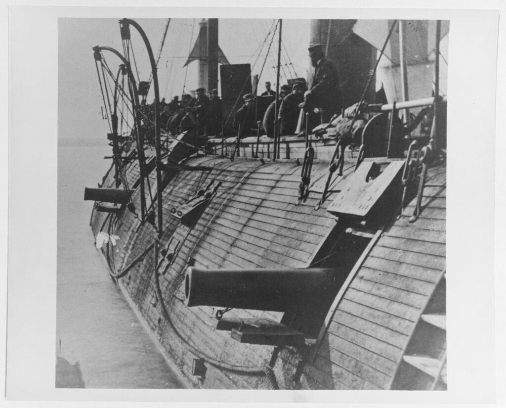 A picture of the side of a ship with cannons visible and people aboard.